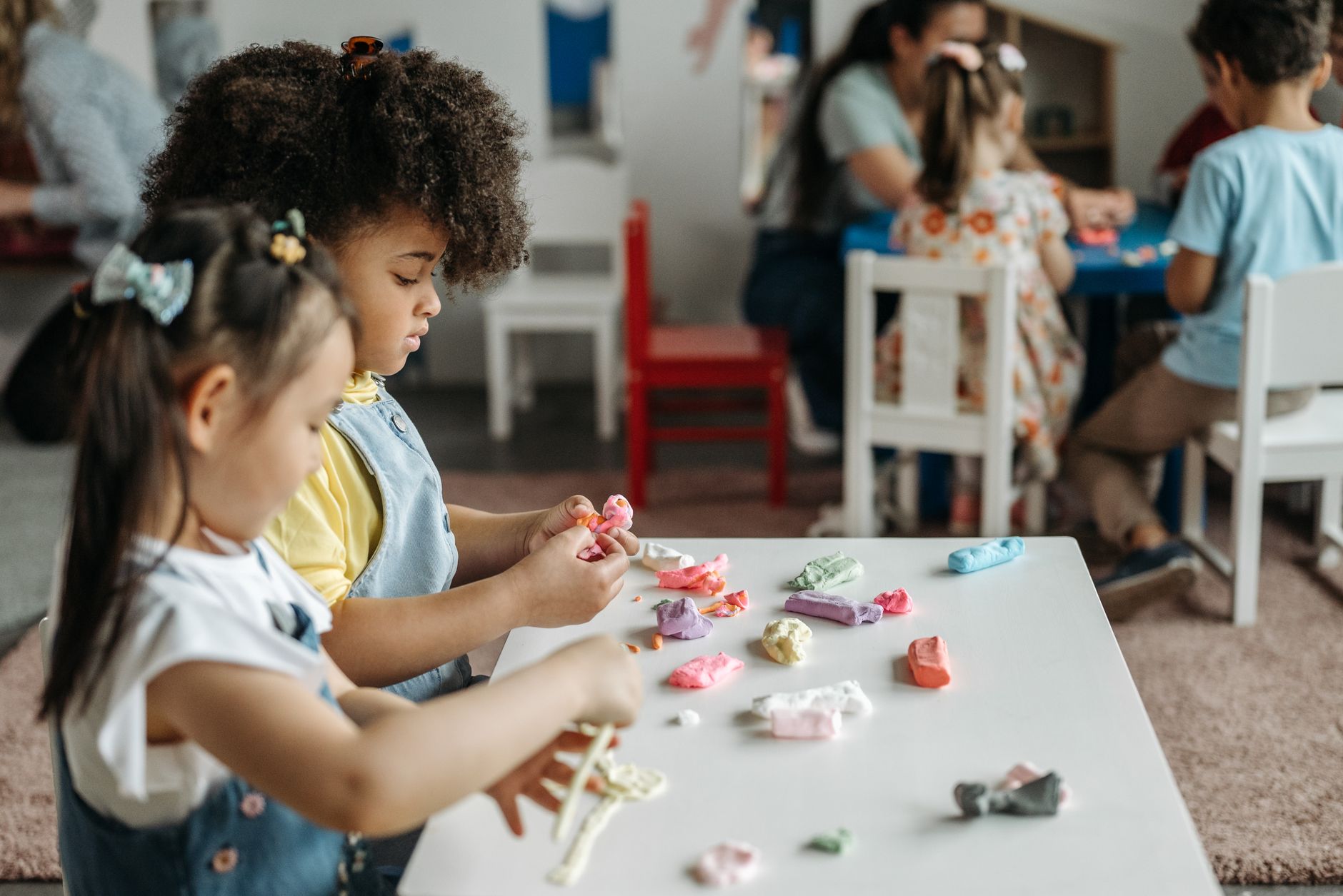 Two children seated at a table exploring modelling clay together