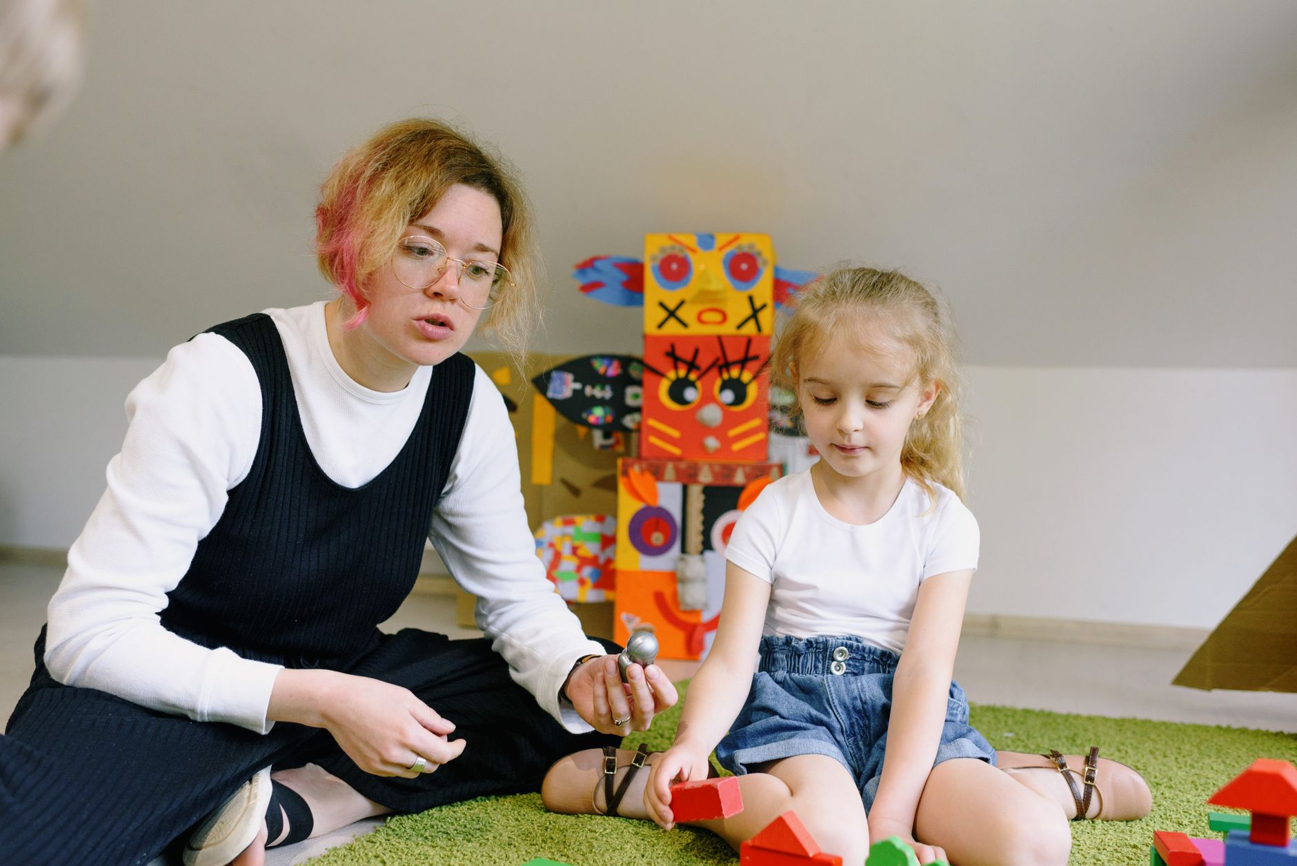 A caregiver and a child playing together with colourful wooden blocks in a calm playroom