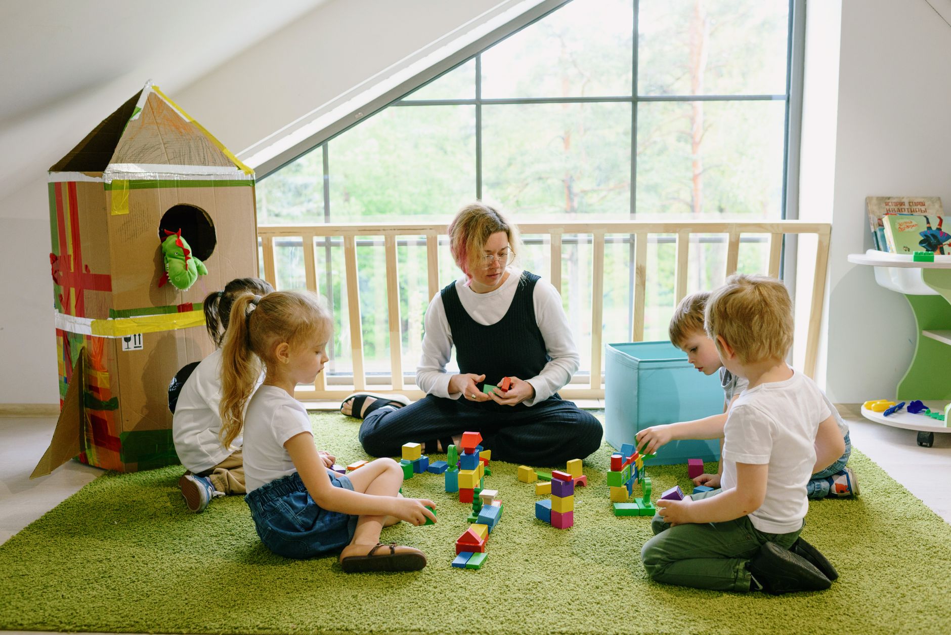 Children quietly playing with wooden blocks and a cardboard house in a naturally lit classroom