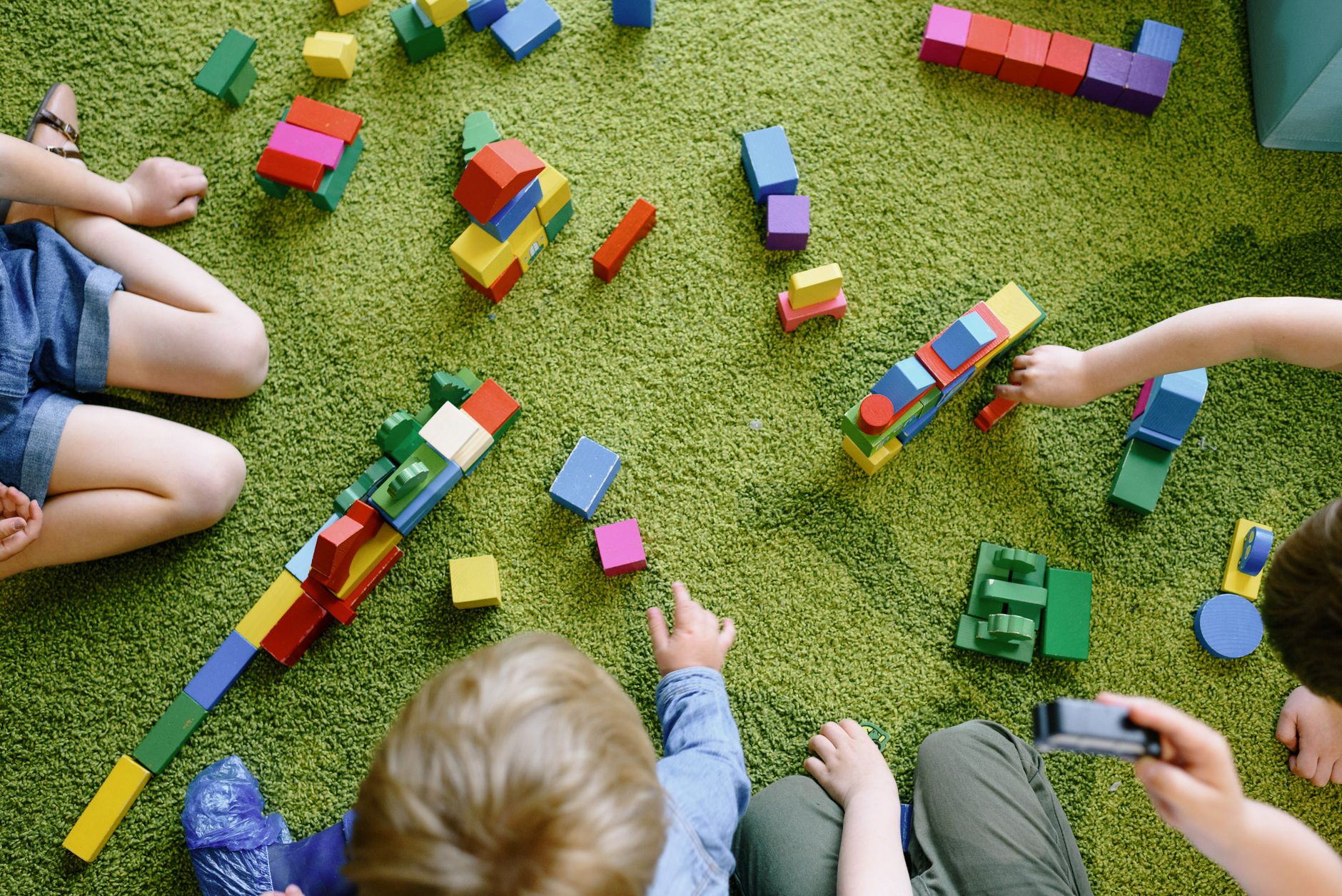 Toddlers playing with colourful wooden blocks on a classroom rug